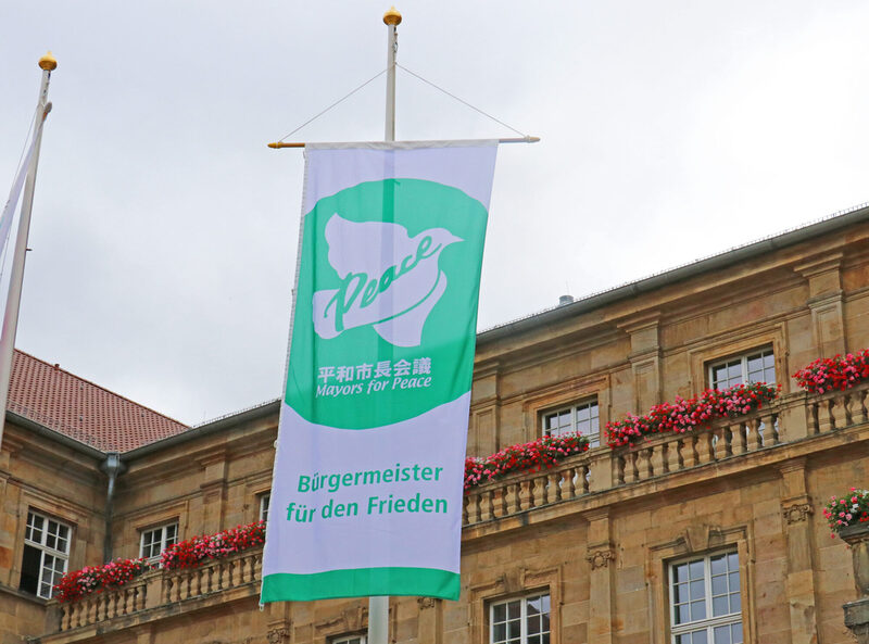 Grün-weiße Flagge mit Friedenstaube und Aufschrift "Bürgermeister für den Frieden"