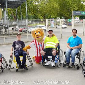 Mehrere Rollstuhlfahrer, die gemeinsam mit einem Maskottchen posieren