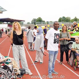 Mehrere Menschen, mit Rollstuhl und stehend, auf einer Rennbahn in einem Stadion