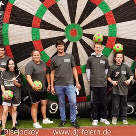 Personen, die vor einer großen Dartscheibe mit Bällen stehen