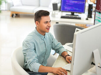 Ein junger Mann sitzt im Büro vor dem Computer und programmiert.