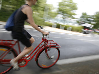 Eine Frau die schnell auf einem roten Fahrrad vorbei fährt