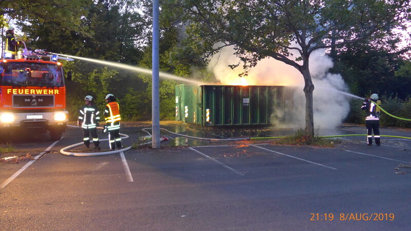 Feuerwehrleute löschen einen brennenden Container