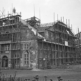 Schwarz-Weiß-Foto mit Blick auf das im Krieg zerstörte Ottoneum. Das Gebäude ist eingerüstet, auf dem Dach steht ein Richtbaum.