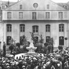 Schwarz-Weiß-Foto des Ottoneum aus der Blickrichtung des heutigen Steinwegs. Eine Menschenmenge steht vor dem Papin-Brunnen, der 1906 eingeweiht wurde.