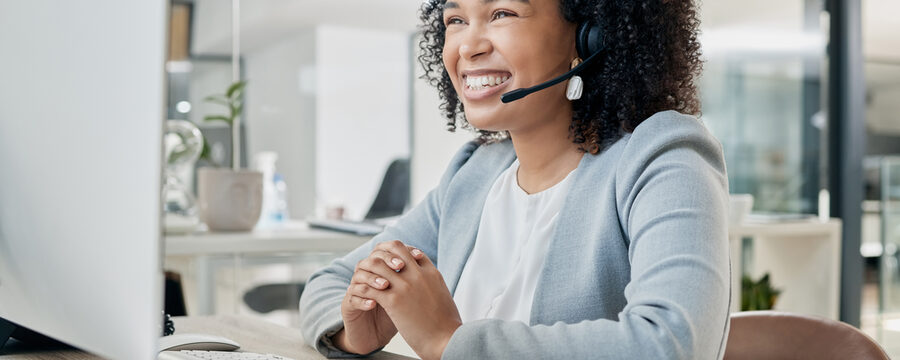 Eine Frau sitzt lächelnd im Büro und ist am telefonieren